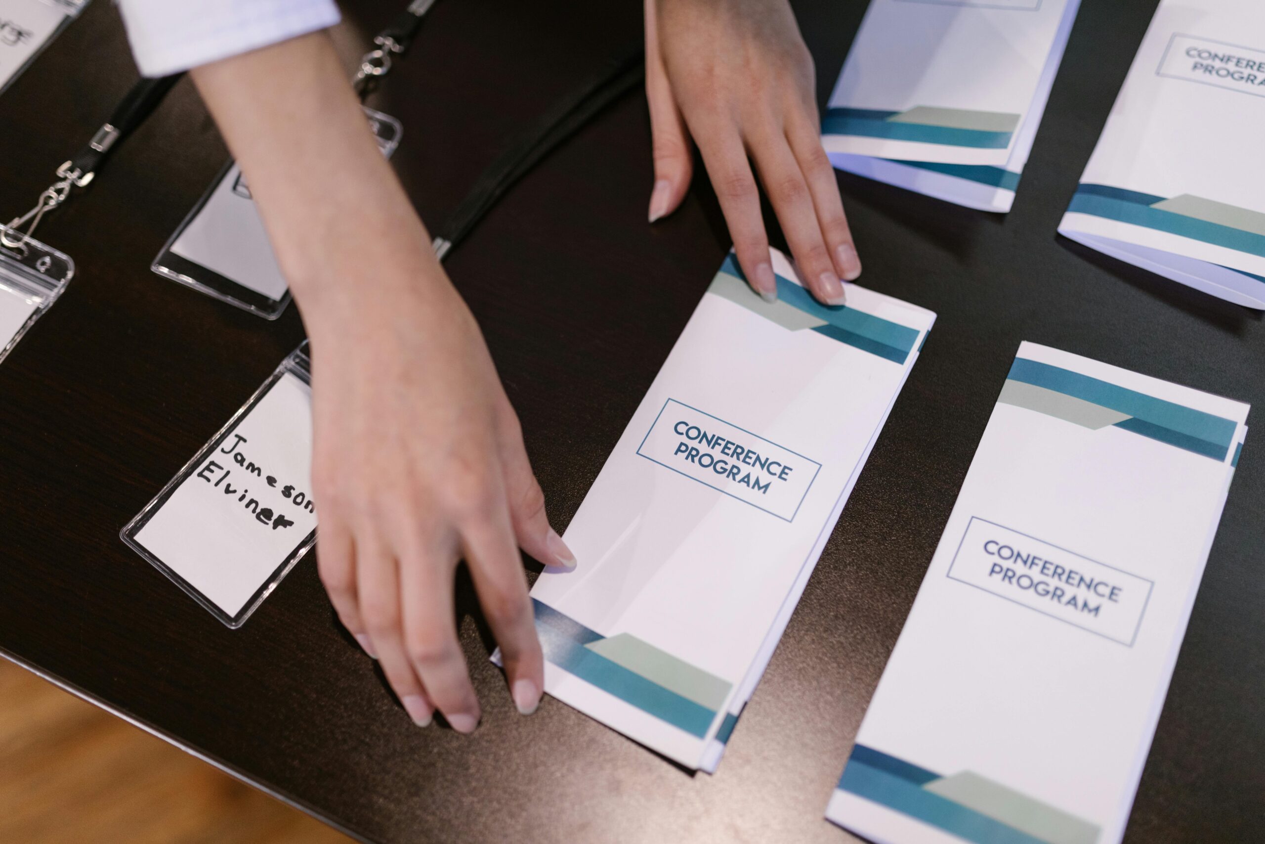 Hands organizing conference programs and name tags at event registration desk.